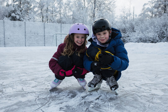 brother and sister ice skating together outside in the snow