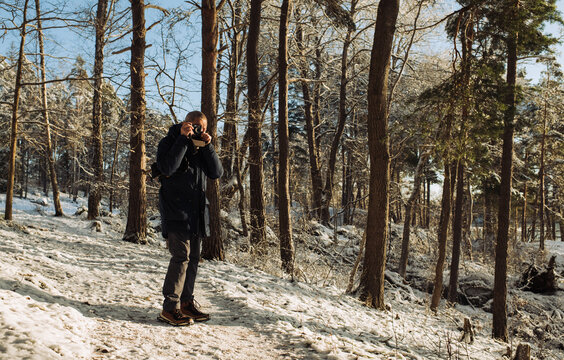 retired man walking in the snow in the forest taking pictures