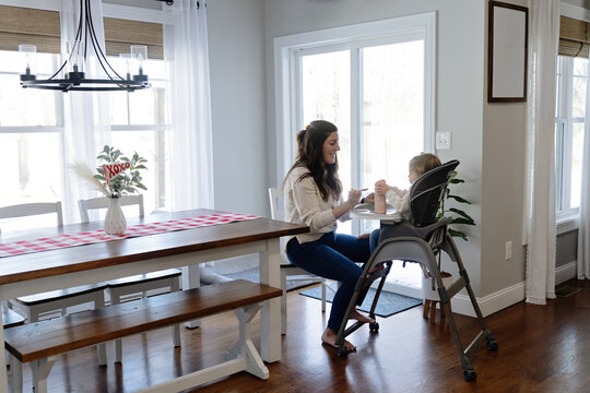 Woman feeding baby lunch while she sits in high chair