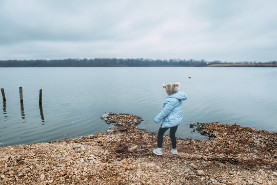 Child throwing rocks into water on shore of lake