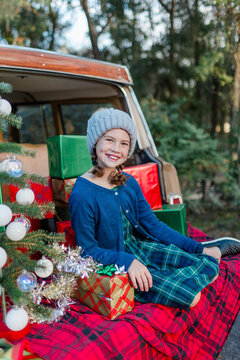 Young girl sits in the back of a vintage vehicle with Christmas gifts