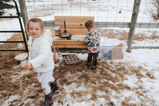 Siblings play in snowy mud kitchen, winter fun