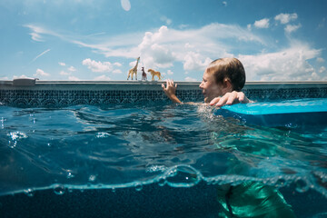 Boy in swimming pool playing with zoo animal toys