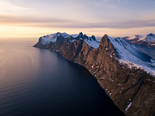 Drone shot of snow covered cliff by ocean at sunset