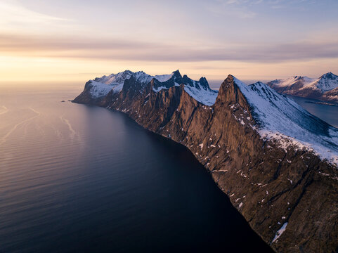 Drone shot of snow covered cliff by ocean at sunset