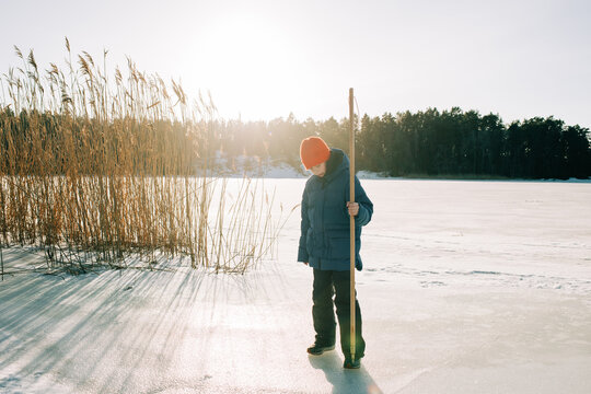 boy using an ice stick to test breaking the ice on a frozen lake