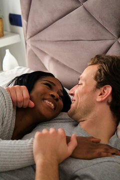 Multiethnic couple in love embracing and lying on bed.