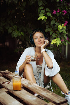 Woman in headphones drinks coffee, cafe, sitting on the lawn. Bali.