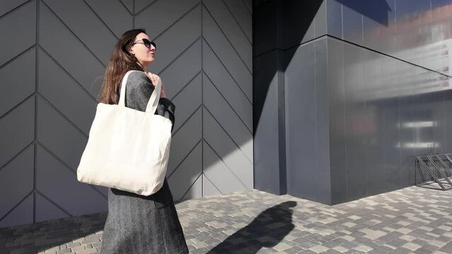 White tote bag or eco cotton bag in woman's hand in urban environment