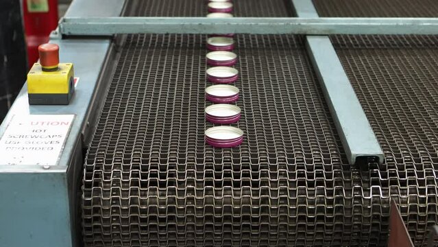 Pink bottle caps on a conveyor belt in a cap lining machine, industrial setting