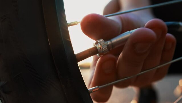 Cyclist screws pump hose with inflator chuck connector to Schrader valve stem, broken punctured wheel. Man will inflate flat tire out of town outside city at sunset. Cross-country mountain bicycle. CU