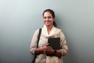 Woman of Indian ethnicity with a smiling face holding a tablet computer in hand - obrazy, fototapety, plakaty