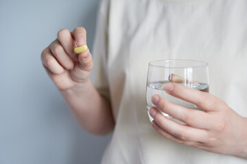 Close-up of female hands holding a pill and a glass of water