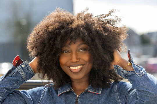 A vibrant portrait of a smiling African American woman with a bountiful afro enjoying the outdoors. The denim attire complements her cheerful demeanor under the open sky, exemplifying a free-spirited