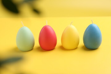 Colorful egg shaped candles on yellow background. Easter decor