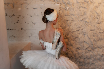 Contemplative ballerina, clad in her feathery white costume, is lost in thought against a textured...