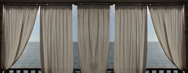 View of sea or ocean from summer terrace or veranda. White curtains shaken by the wind. Blue sky with cloud in summer. Blurred photo background, front view. curtains blowing in wind at tropical resort