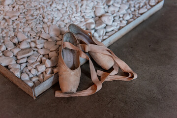 Pair of used ballet slippers rests on pebble-covered surface, hinting at the rigorous practice behind a dancer's journey. © farmuty