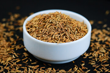 Cumin seeds in a white bowl on a black wooden table.