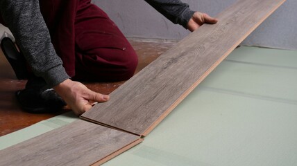 joining two planks of laminate with a wood pattern on the floor and laying the covering on a green insulating backing, a worker lays laminate on the floor in a room