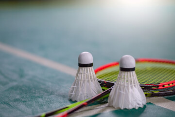 Cream white badminton shuttlecock and racket with neon light shading on green floor in indoor badminton court, blurred badminton court background, copy space.	