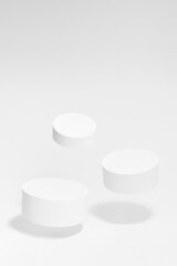 Set of three round white pedestals mockup for cosmetic products, tilt, fly in hard light, shadow on...