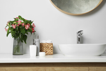 Vase with beautiful Alstroemeria flowers and toiletries near sink in bathroom
