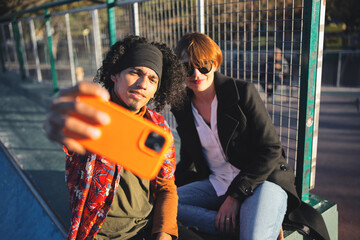 Fashionable multiracial couple having fun together in a skate park. Couple taking selfie portrait...