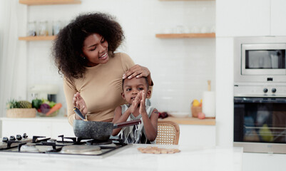 Multiracial mother and son have fun cooking food together in kitchen at home. Young multiethnic...