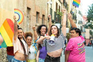 A transgender is holding a megaphone and is surrounded by a group of people. The group appears to be celebrating something, possibly a gay pride event. The transgender is the center of attention