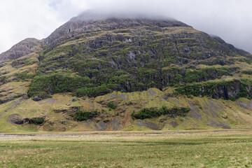 Majestic mountain draped in greenery under a cloud-capped peak, as viewed from the lush valleys...