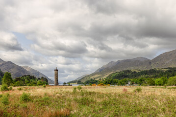 Overlooking the tranquil waters of Loch Shiel, the historic Glenfinnan Monument is framed by the rolling hills of the Scottish Highlands, under a vast, expressive sky