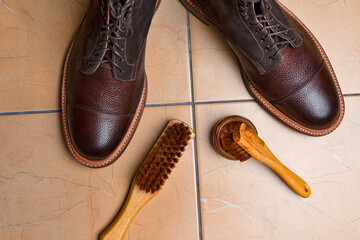 Closeup View of Various Shoes Cleaning Accessories for Dark Brown Grain Brogue Derby Boots Made of Calf Leather Over Tile Background - 770486192