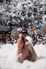 Woman at foam party by pool, epitomizing resort fun. Perfect for resort hotels, entertainment complexes, party supplies, cosmetics, and bathing essentials.