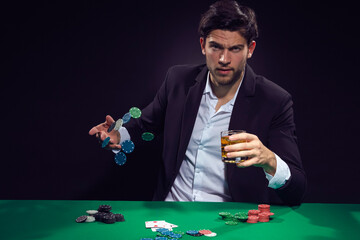 Addiction Ideas. Emotional Handsome Caucasian Brunet  Pocker Player At Pocker Table With Chips and Cards Playing and Drinking Alcohol While Throwing Chips.