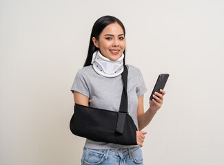 Happy young asian woman broken arm holding smartphone. Woman put on plaster cast splint with walking sticks crutches. Patient wearing sling support arm with neck collar. life insurance and accident