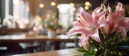 Fotobehang A beautiful bouquet of pink lilies, a type of flowering plant, is elegantly displayed on a wooden table in a cozy restaurant setting © AkuAku