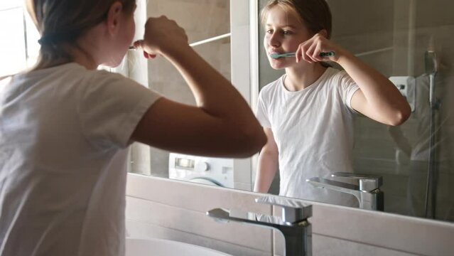 Little Girl Brushing Her Teeth In The Bathroom Mirror In The Morning Before School