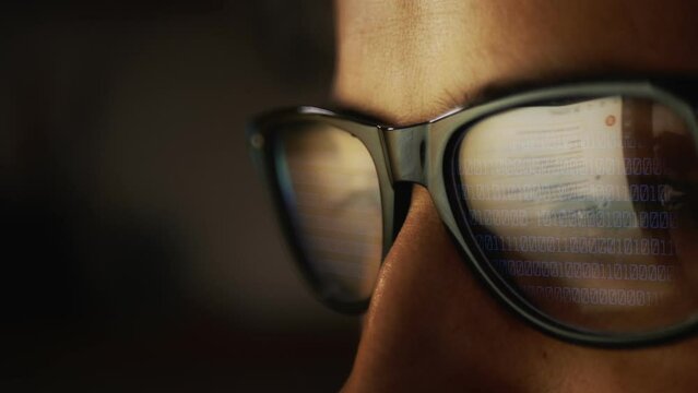 In the reflection of glasses on a male face, surfing the Internet and rows of binary code numbers. Cg