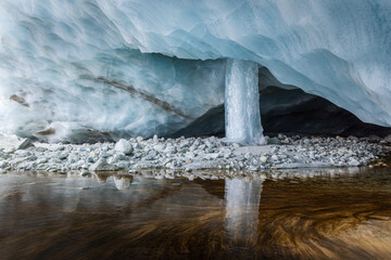 Glacier ice cave with a frozen waterfall reflecting in the water in Zinal Wallis, Switzerland