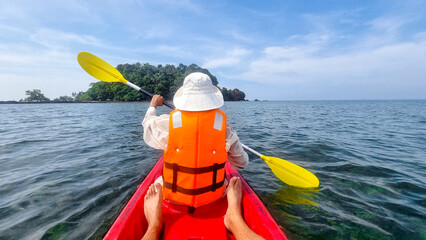 A person in a kayak paddles towards a small island, surrounded by calm waters and green foliage...