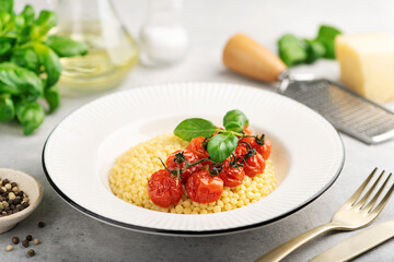 Pasta ptitim with cherry tomatoes and basil in a white plate