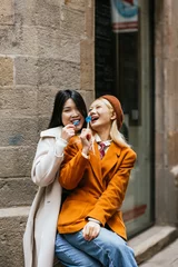 Fotobehang Asian lesbian couple having fun while eating lollipops together outdoors. © Jordi Mora