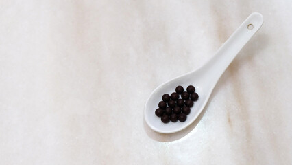 White soup spoon, with traditional Chinese medicine in form of small black balls. On marble surface and copy space on the left.
