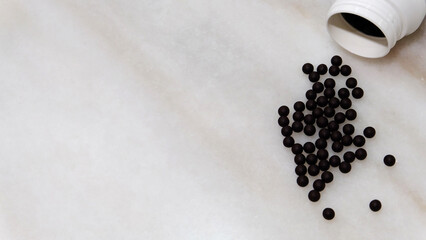 Traditional form of Chinese medicine in small black balls. On marble surface, with copy space on the left.