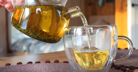 Tea drink is poured from teapot into glass mug on table. Morning tea ceremony, moment of pleasure....