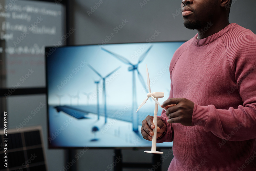 Poster cropped shot of young male manager with model of windmill in hands standing against interactive boar