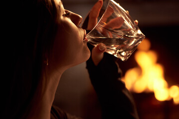 Beautiful girl with red lipstick drinks alcohol near the fireplace