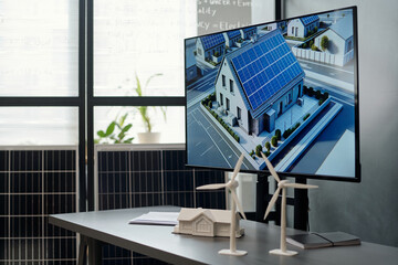 Models of windmills and house on desk with visual template of new residence with solar panels on...