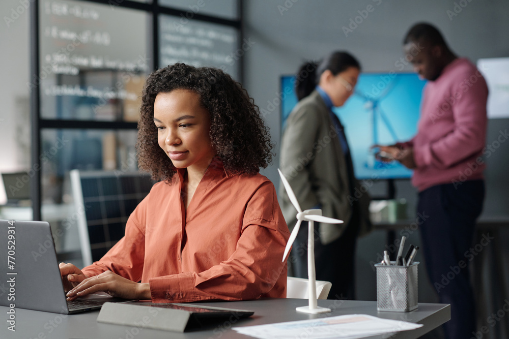 Poster young serious businesswoman touching keys of laptop keyboard and looking at screen while searching f